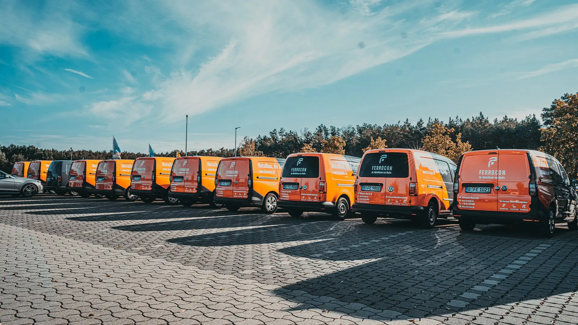 Einheitlich folierte Ferrocon Fahrzeugflotte in Orange und Anthrazit in Reihe auf dem Firmenparkplatz